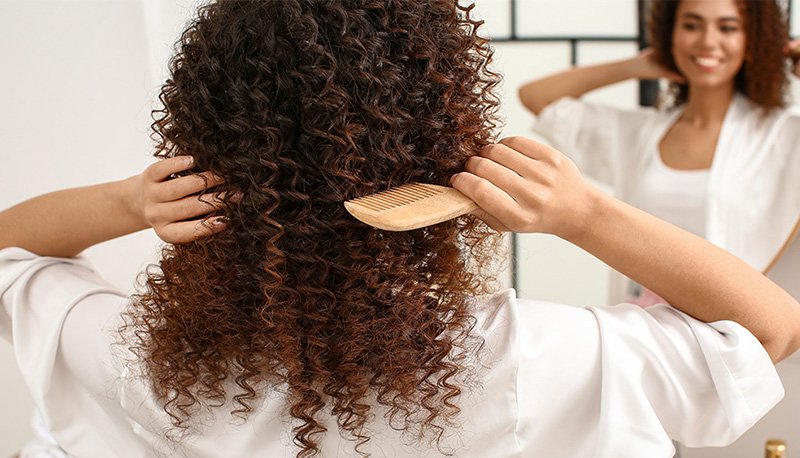 kobieta czesząca końcówki nawilżonych, kręconych włosów